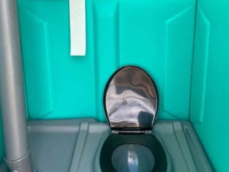 Interior of a teal portable restroom after service, with a clean seat, wiped walls and fresh blue water