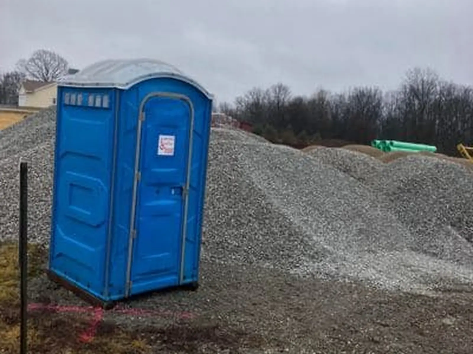 A blue Rockin L portable toilet staked beside a gravel stockpile on an active Indiana construction site