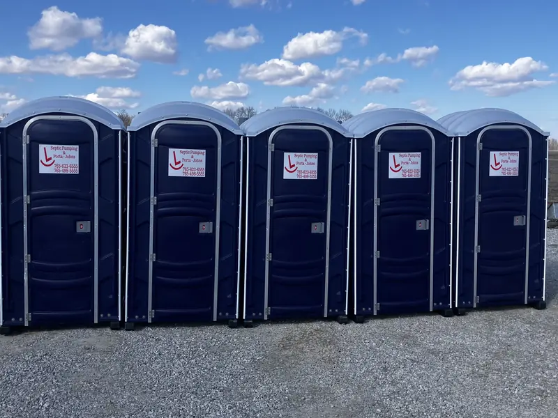 Five blue Rockin L portable restrooms on a gravel lot under a clear blue sky