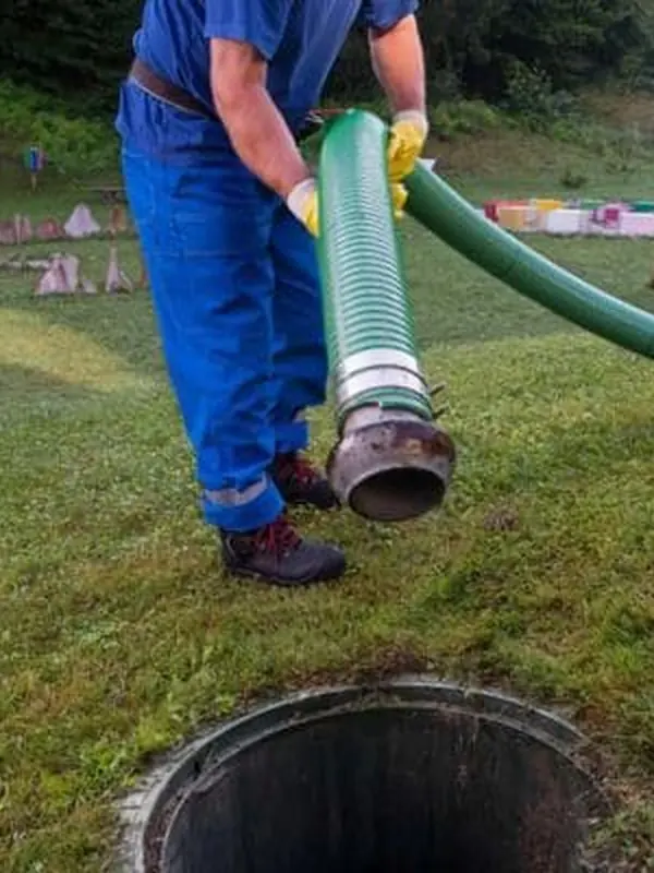 Dane Leatherman in blue coveralls lowering a suction hose into an open septic tank lid