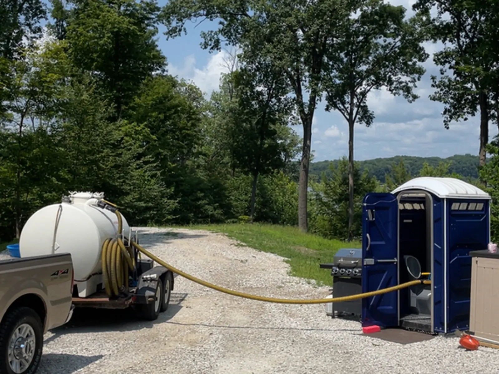 Rockin L vacuum tank rig set up on a gravel driveway with hose running toward a rural Indiana home's septic access