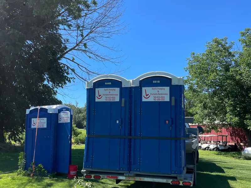 Two Rockin L portable restrooms strapped to a delivery trailer parked on a green lawn
