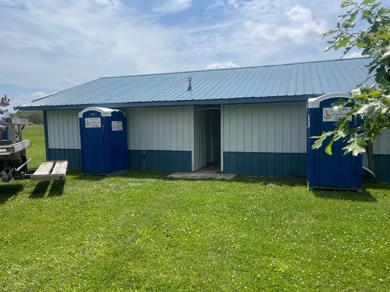 A pair of blue portable restrooms set beside a green and cream pole barn on an Indiana property