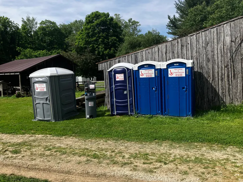 Three blue Rockin L restrooms set along a weathered barn wood fence line at a rural Indiana property