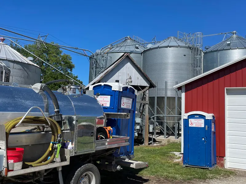 Rockin L stainless vacuum tank truck parked beside grain bins and a red barn on a west-central Indiana farm